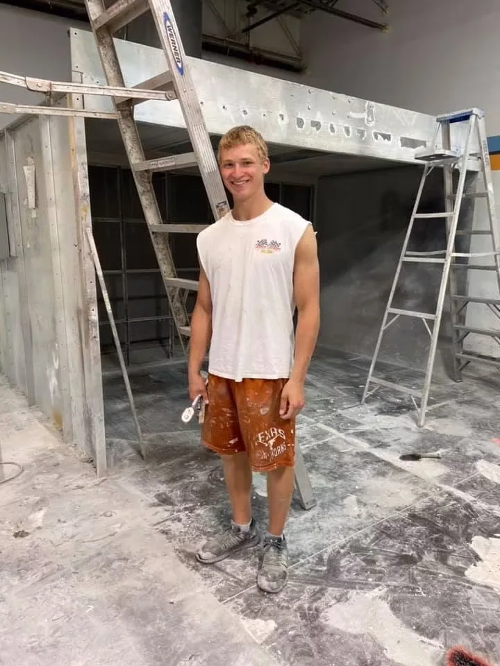 Me at around age 16 standing at a job site with ladders and work materials behind me.